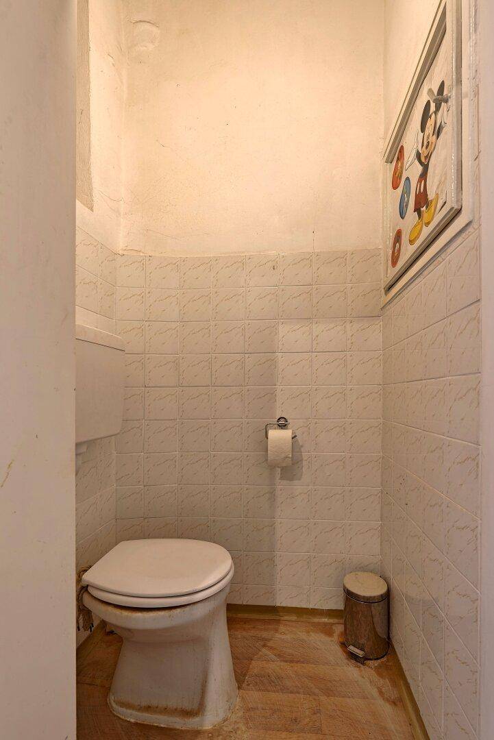 Kleines WC mit weißen Fliesen an den Wänden und einer Toilette.