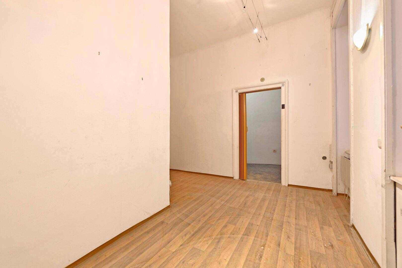 Leerer Raum mit Laminatboden und einem Durchgang zu einem weiteren Zimmer.