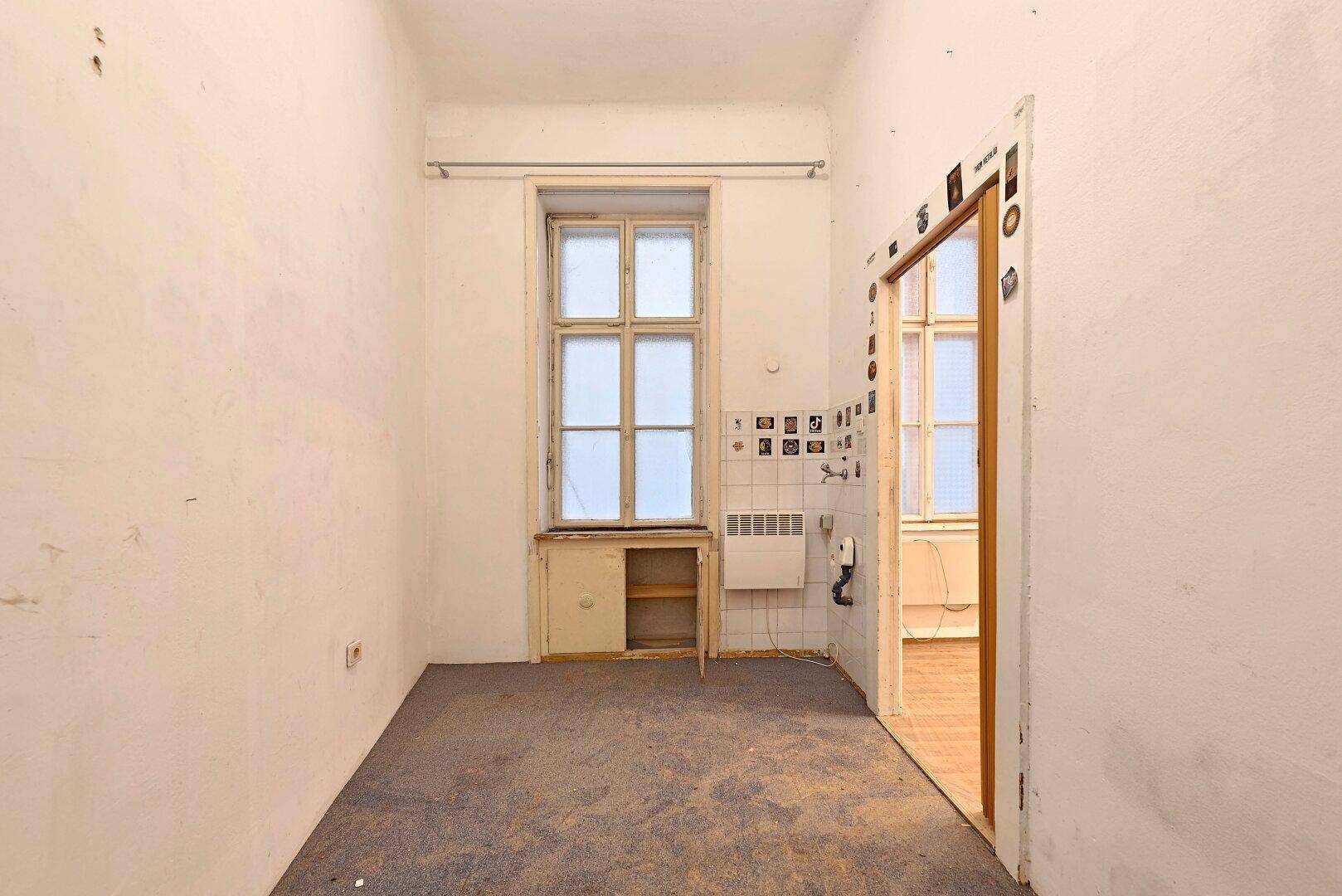 Leerer Raum mit Teppichboden, einem Fenster und einem kleinen Einbauschrank.