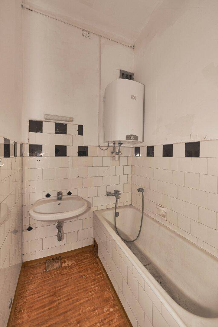 Badezimmer mit weißen und schwarzen Fliesen, einer Badewanne, einem Waschbecken und einem Warmwasserboiler.