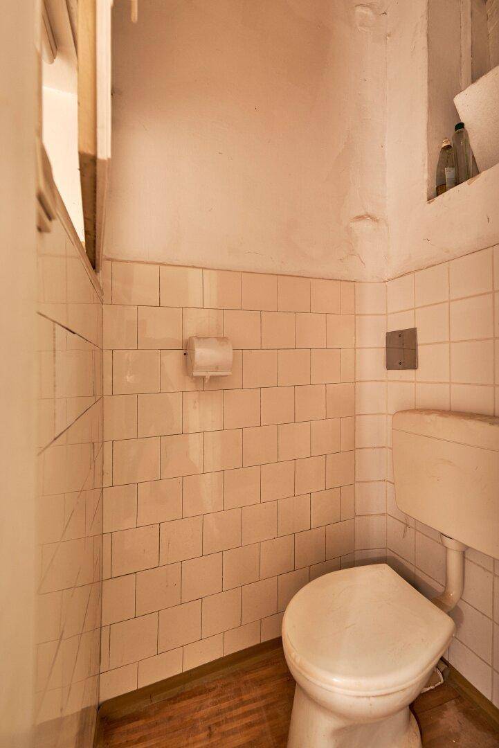 Einfaches WC mit hellen Fliesen an den Wänden und einem Holzfußboden.