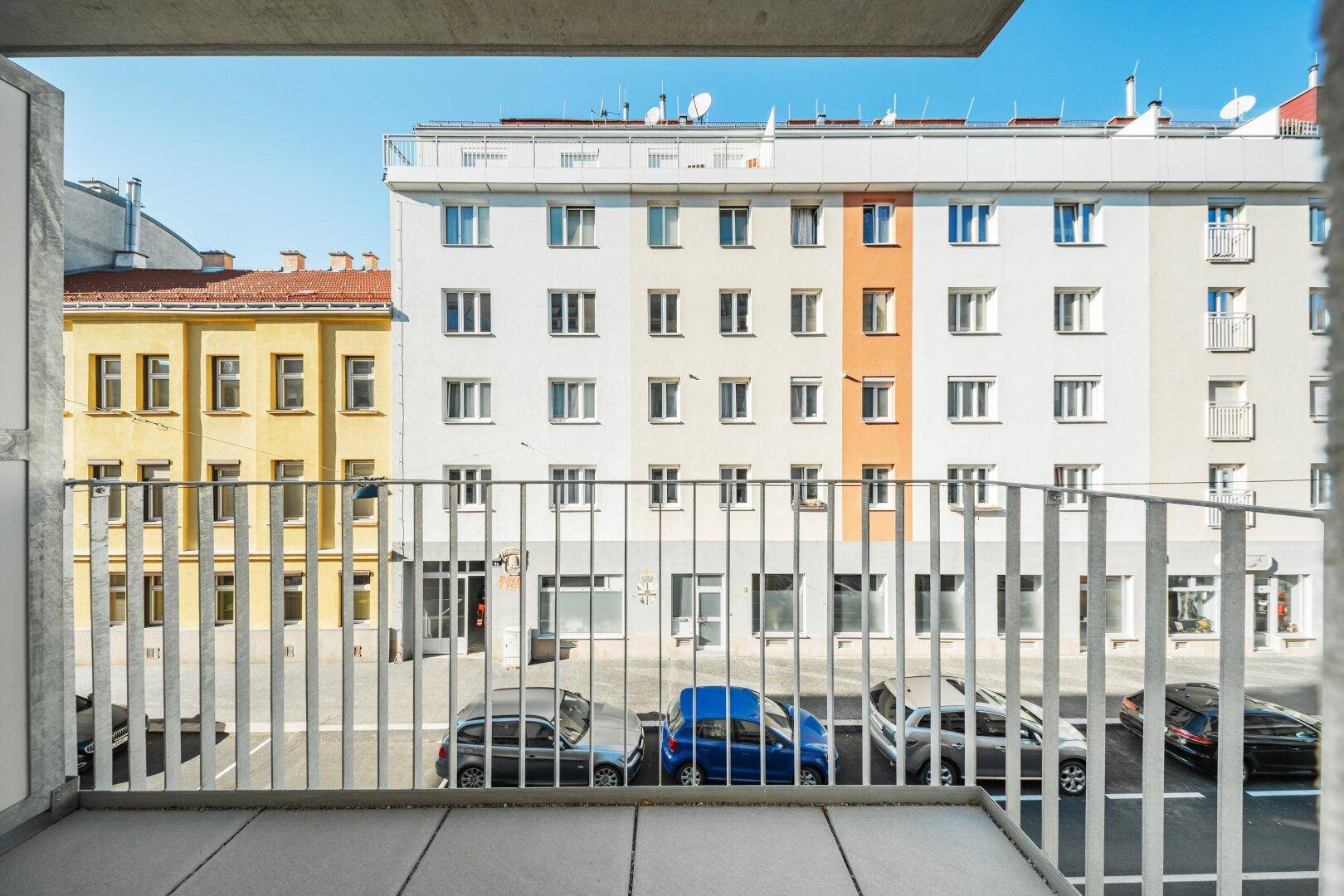 Balkon mit Blick auf die Straße und umliegende Wohngebäude, sonniger Außenbereich.