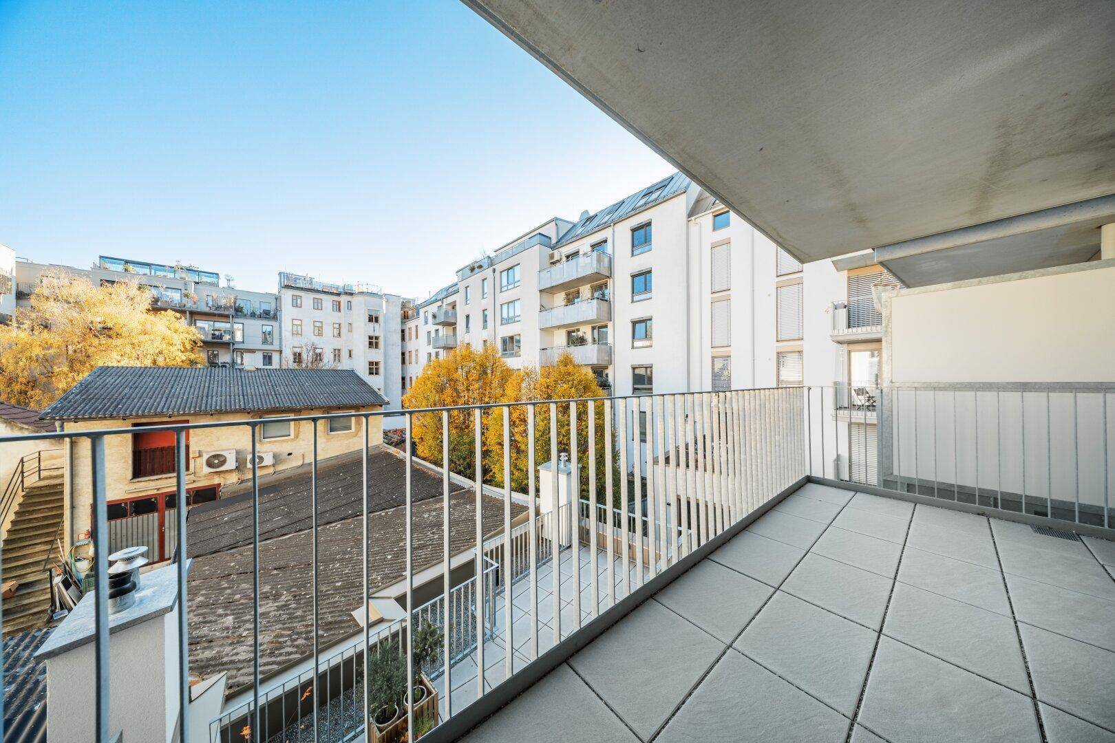 Heller Balkon mit Fliesenboden und weitem Blick auf die umliegenden Gebäude und Bäume.