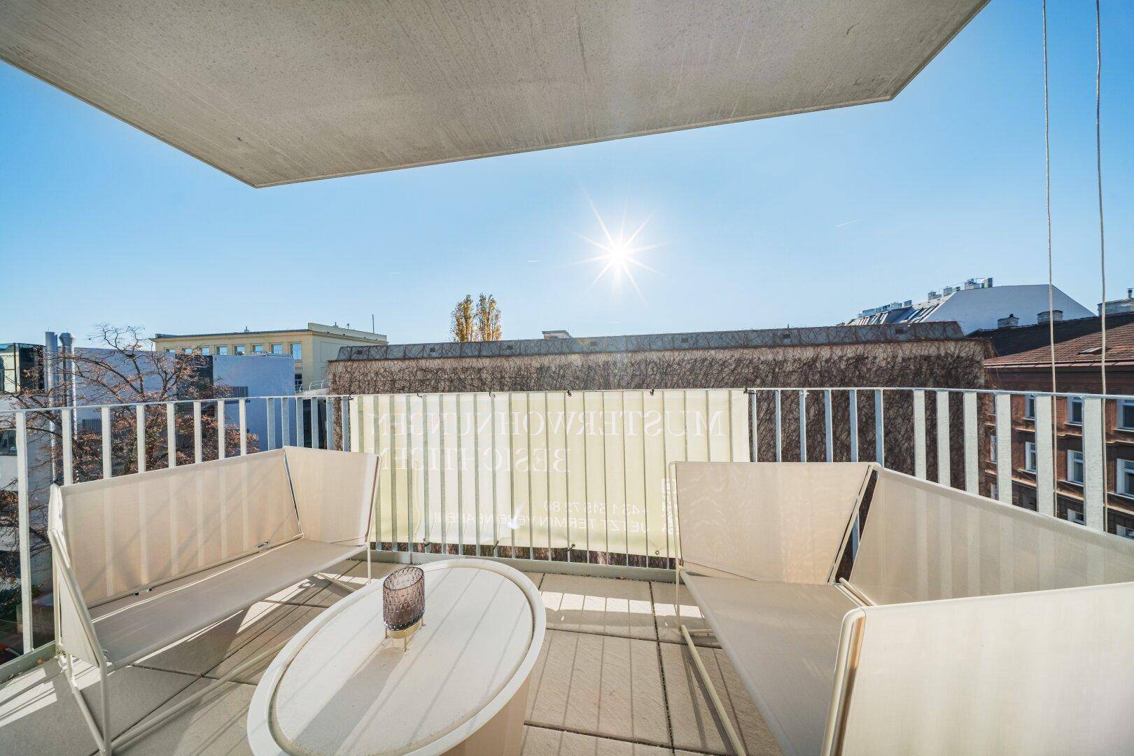 Geräumiger, sonniger Balkon mit bequemen Outdoor-Sitzmöbeln und Blick auf die umliegenden Gebäude.