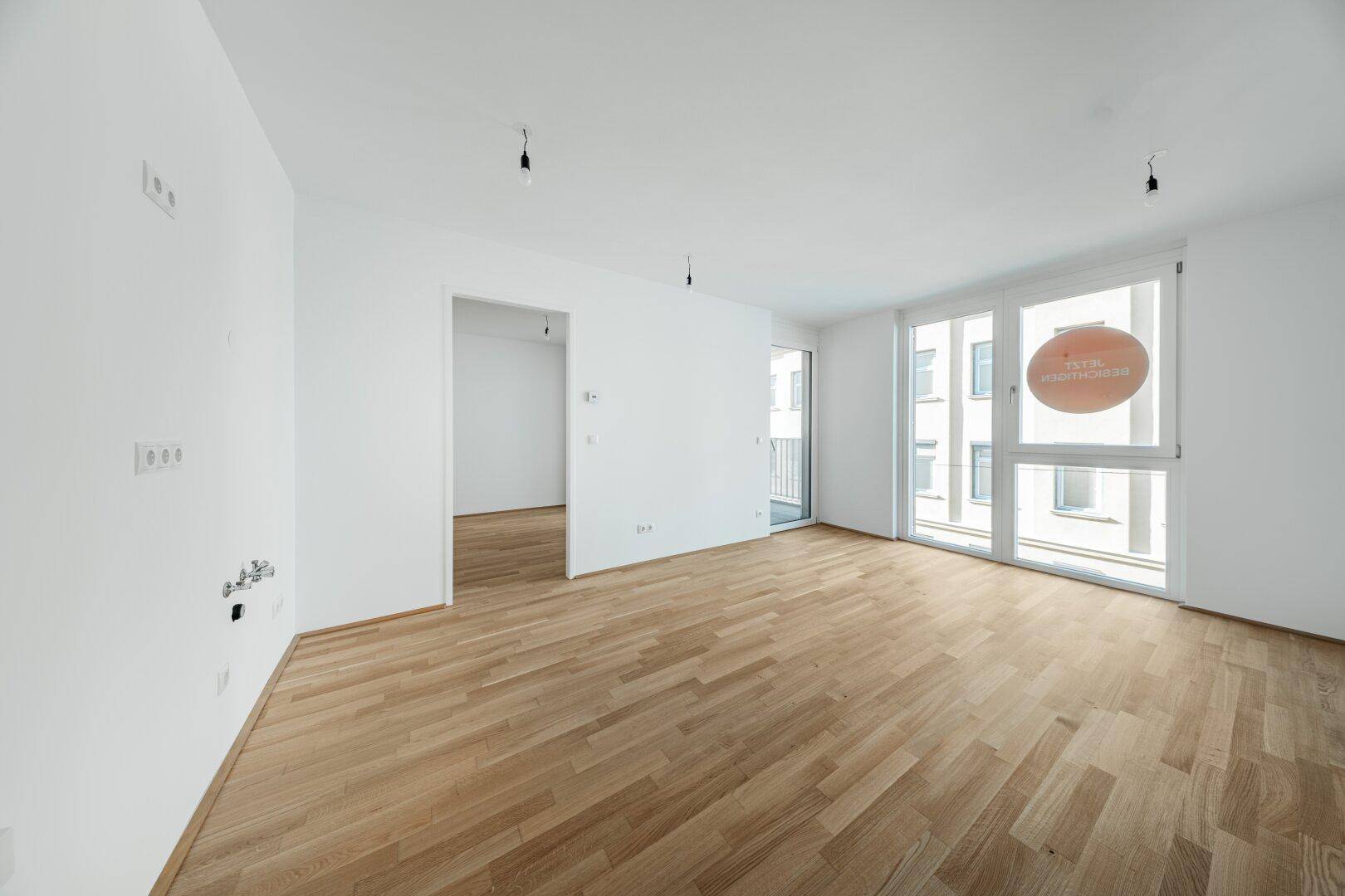 Heller, leerer Wohnraum mit Parkettboden und großem Fenster, bereit zur individuellen Gestaltung.