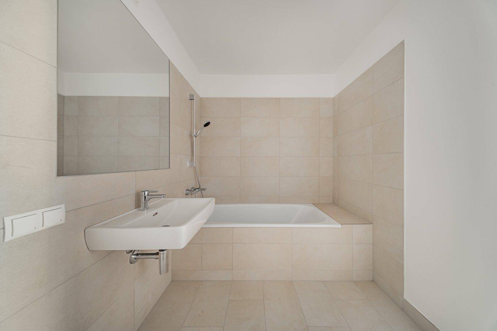 Modernes Badezimmer mit Badewanne, Waschbecken und hellen Fliesen an Wänden und Boden.