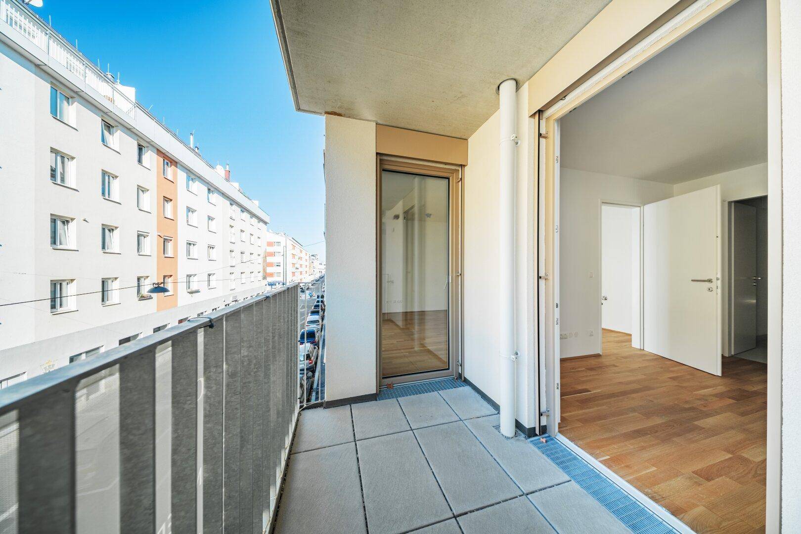Langer Balkon mit Fliesenboden und Blick auf die Straße und angrenzende Gebäude.