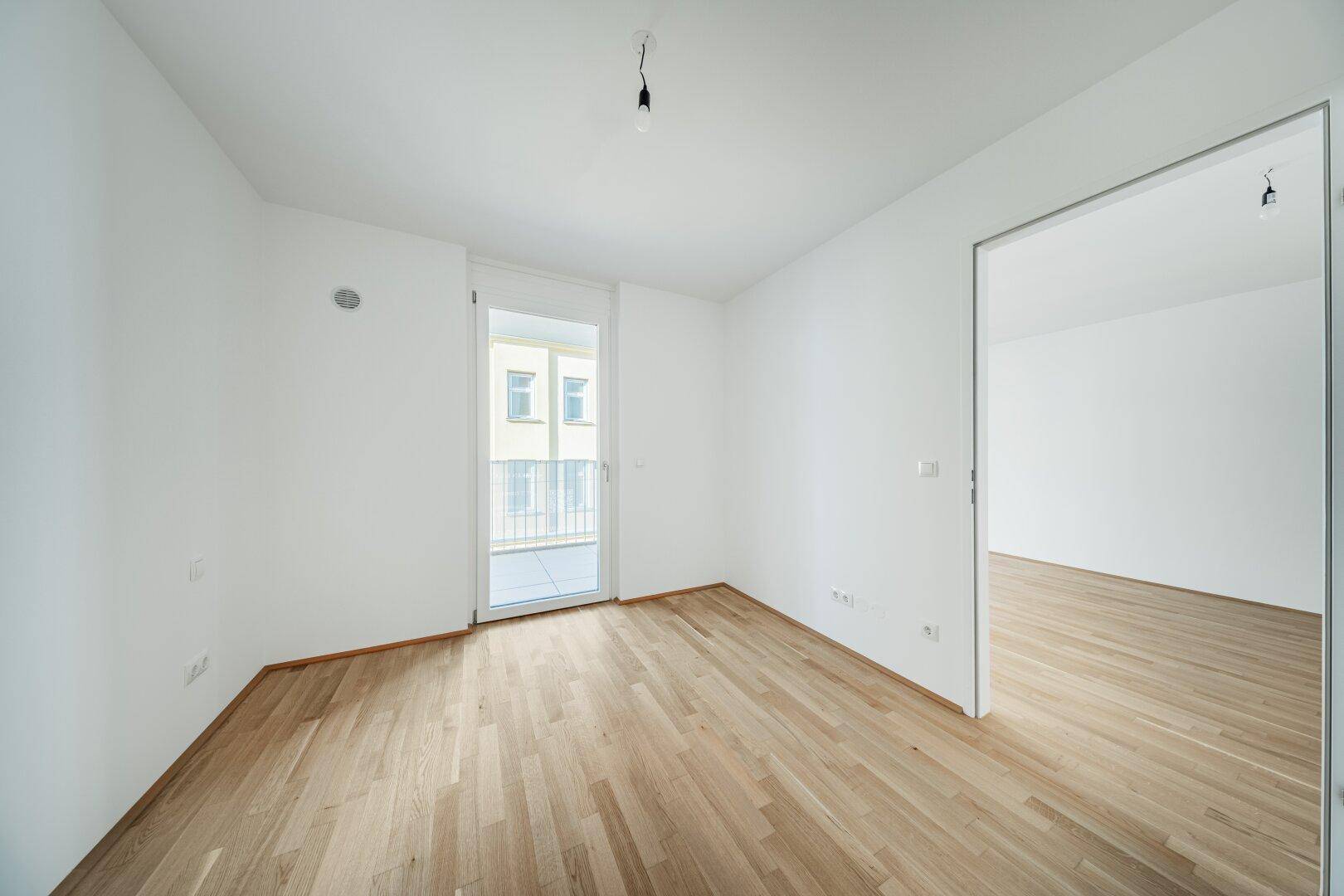 Leerer Raum mit Parkettboden und Zugang zu einem kleinen Balkon, ideal als Schlafzimmer.