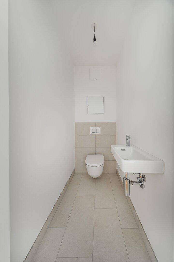 Modernes Gäste-WC mit wandhängender Toilette und Waschbecken, gefliestem Boden und Wänden.