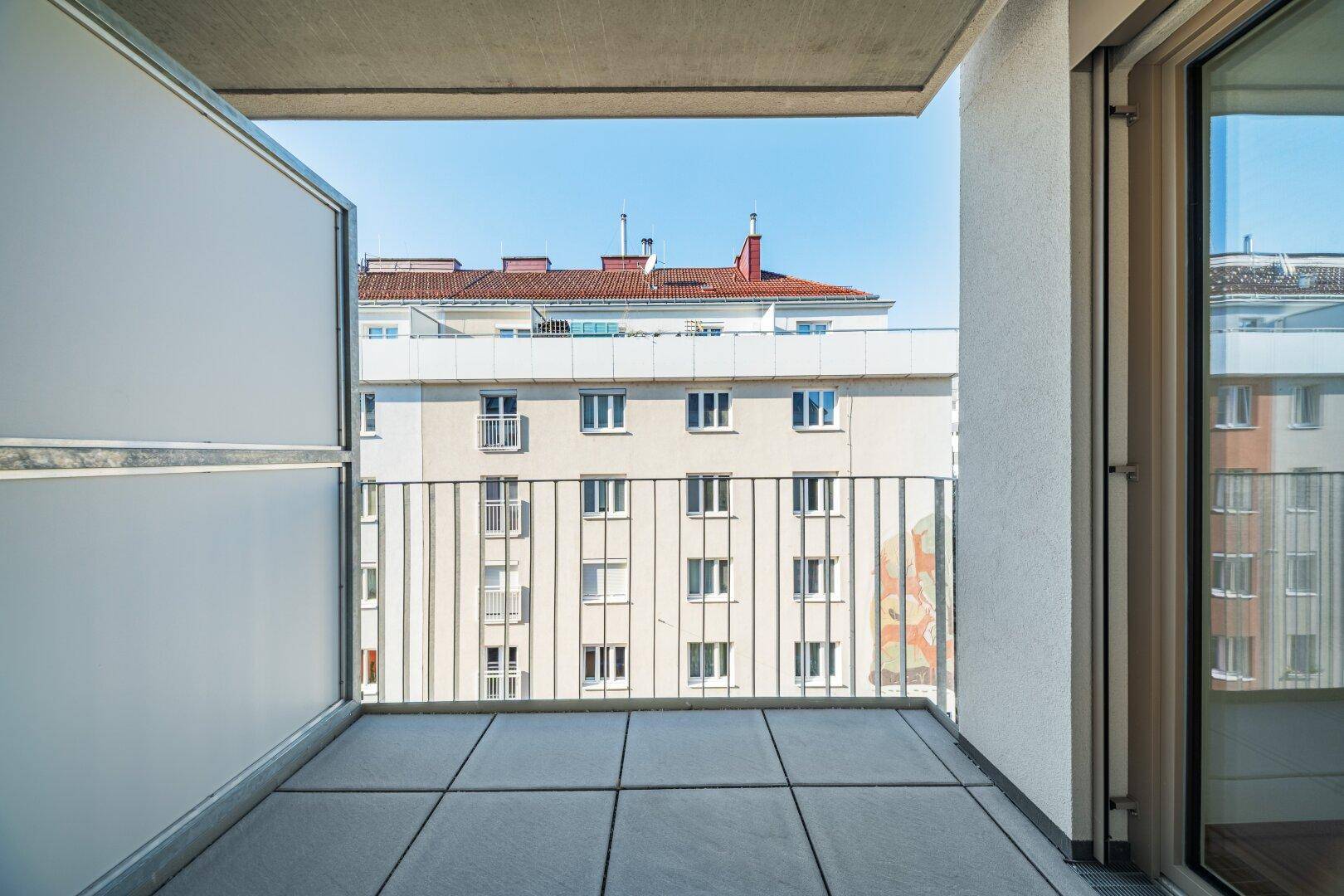 Heller Balkon mit Fliesenboden und Blick auf die umliegenden Gebäude der Stadt.