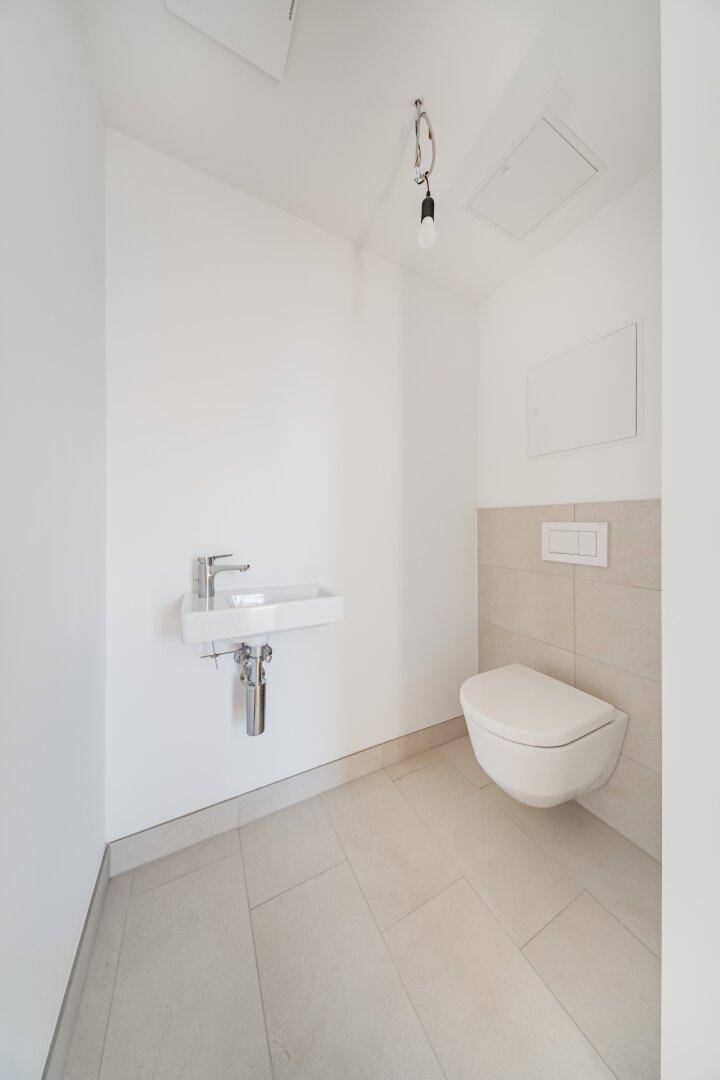 Modernes Gäste-WC mit wandhängender Toilette, kleinem Waschbecken und hellen Fliesen.