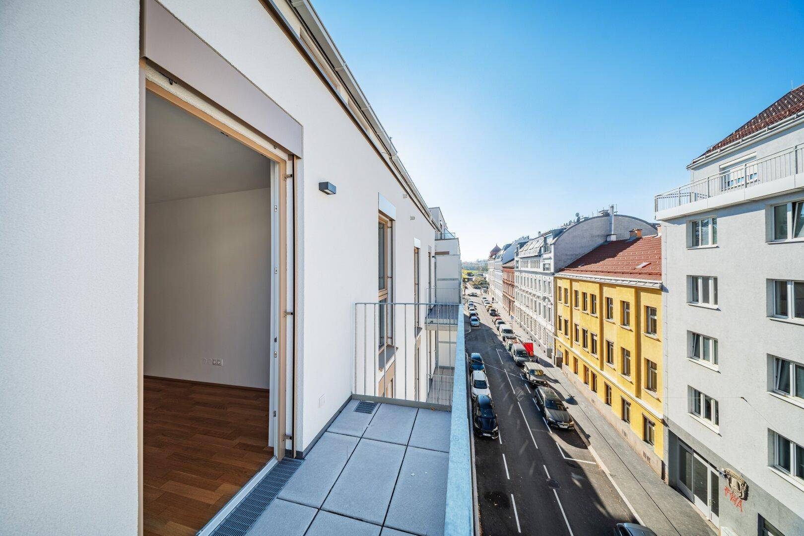 Balkon mit Fliesenboden und Blick auf die belebte Straße und umliegende Gebäude.