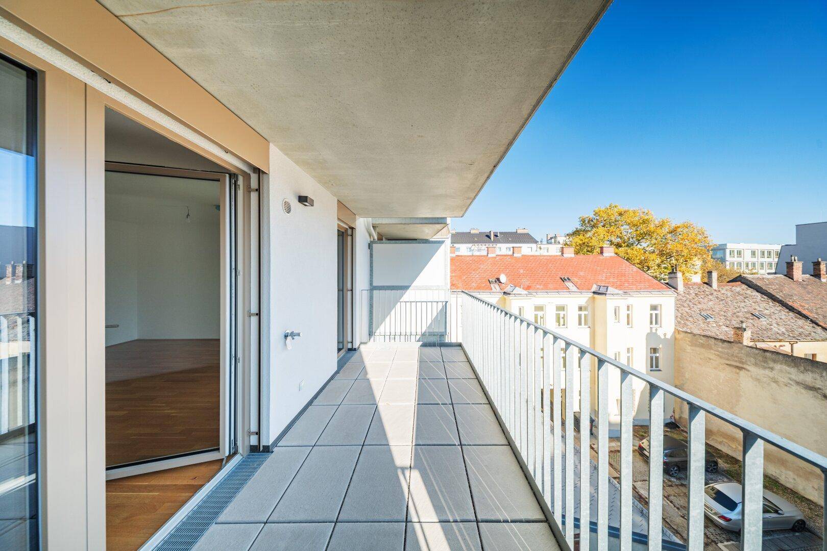 Langer Balkon mit Fliesenboden und Blick auf die umliegende Wohnbebauung.