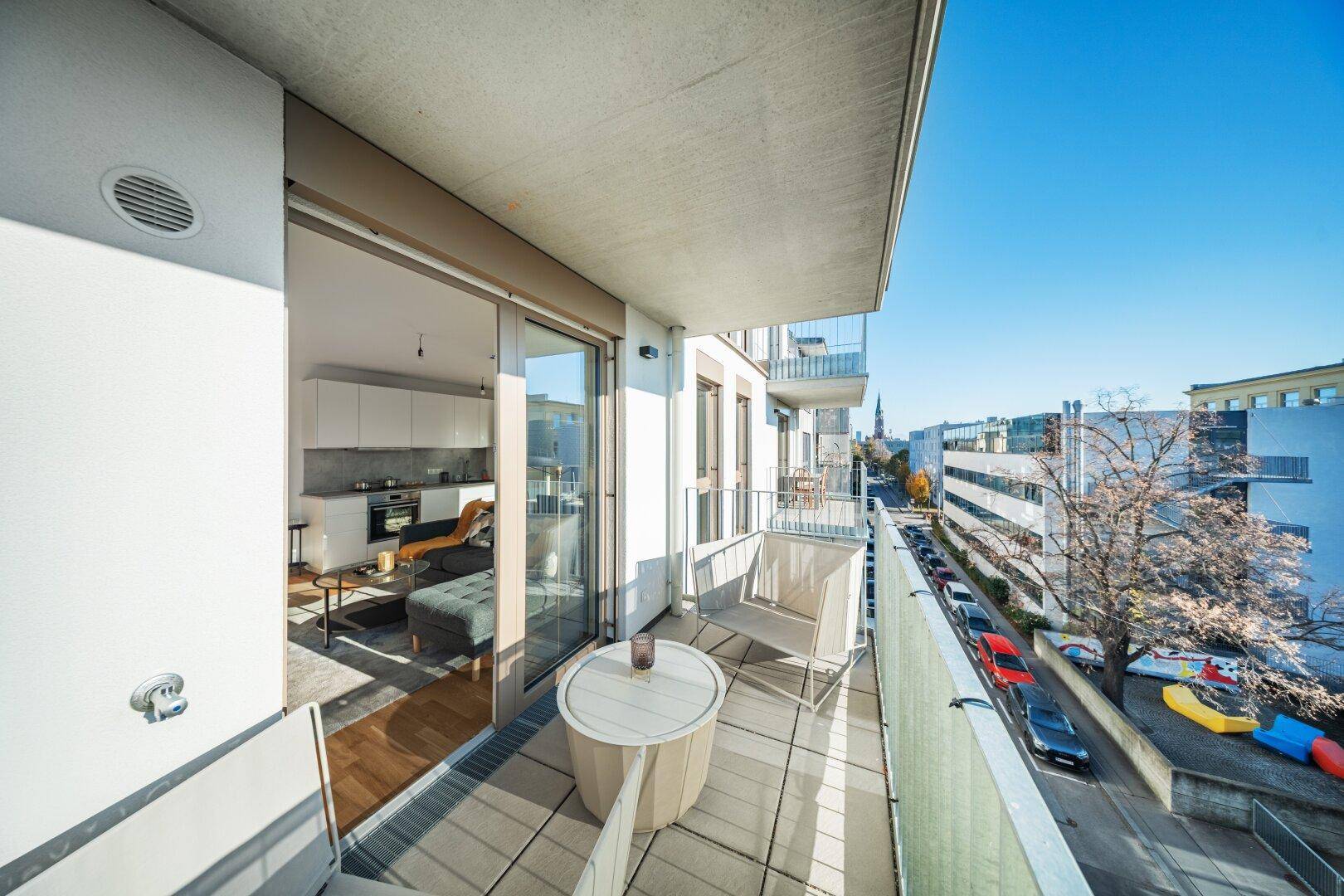 Schmaler Balkon mit Sitzgelegenheiten und Blick auf die Straße und umliegende Gebäude.
