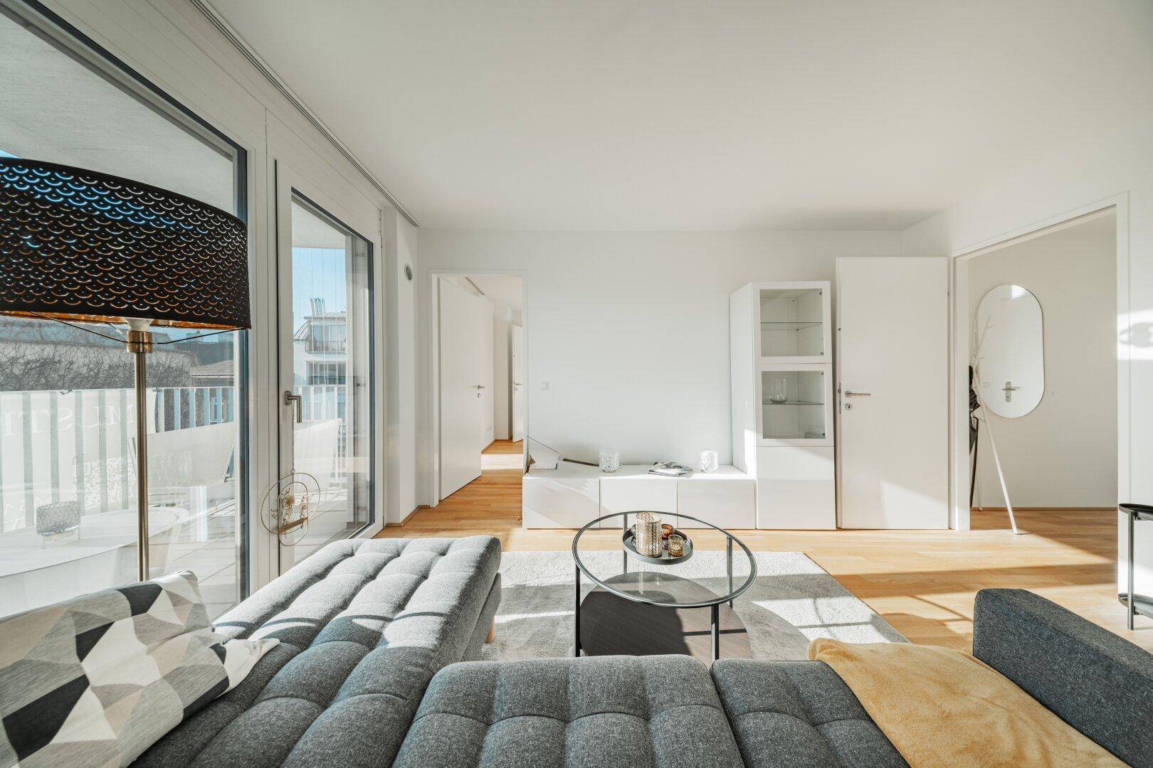 Helles Wohnzimmer mit Holzboden und großzügigen Fenstern, die viel Tageslicht hereinlassen.