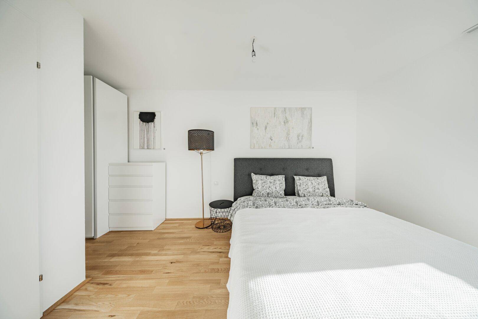 Helles Schlafzimmer mit Holzboden, modernem Bett und minimalistischer Einrichtung.