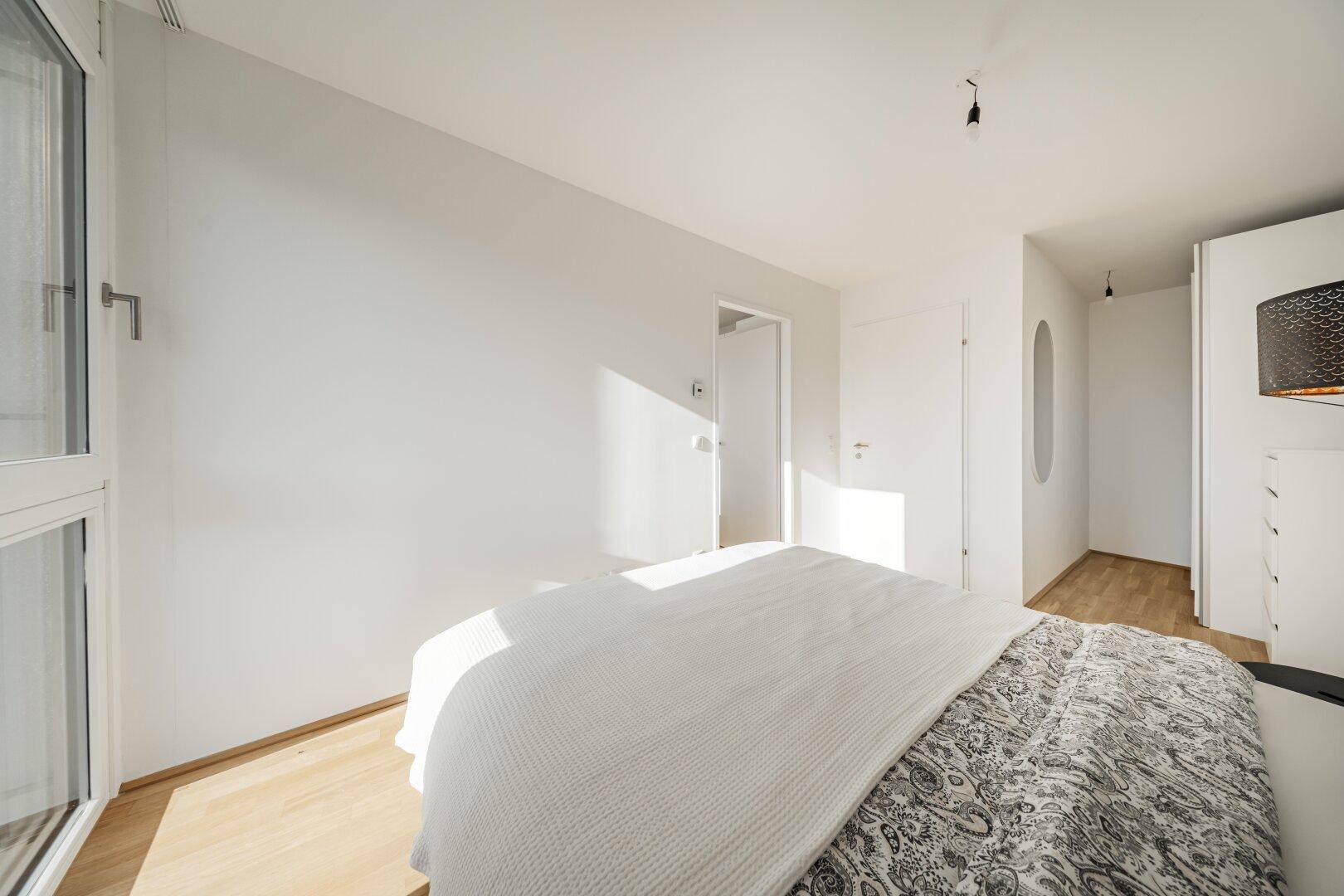 Sonniges Schlafzimmer mit Holzboden und Zugang zu einem weiteren Raum oder Flur.