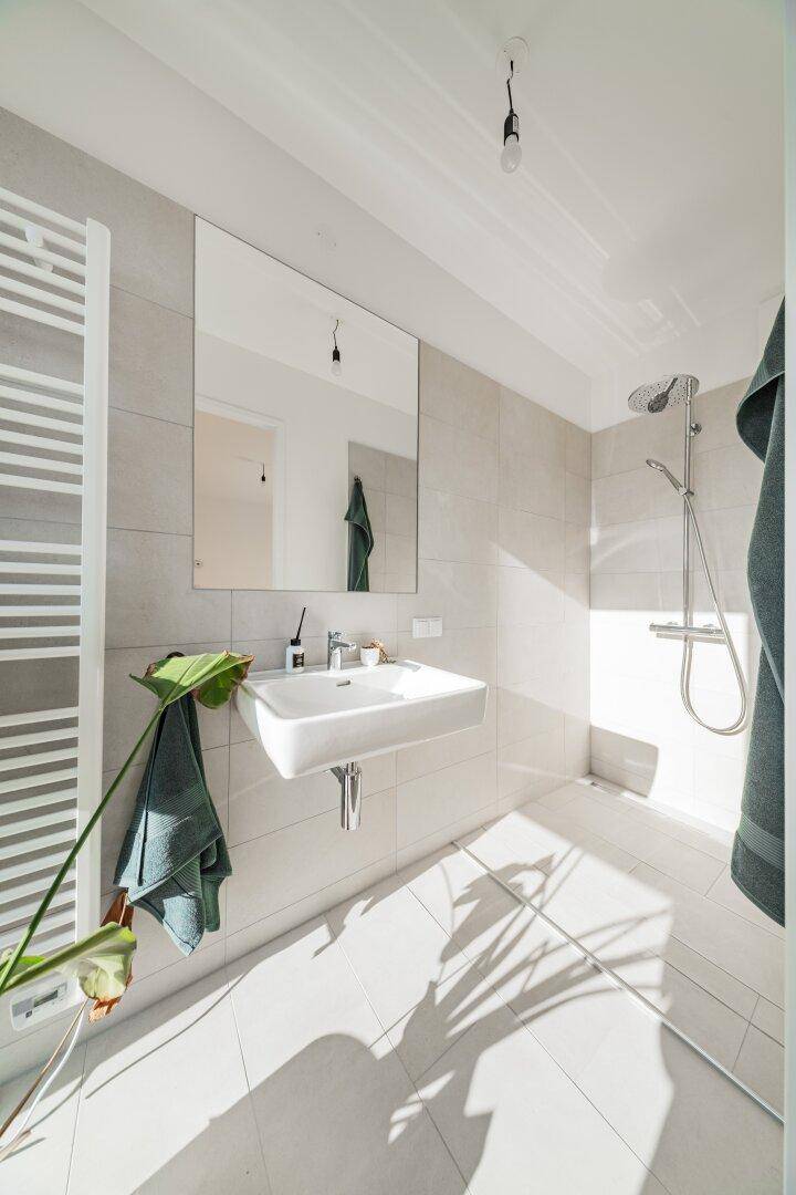 Modernes Badezimmer mit ebenerdiger Dusche, schwebendem Waschbecken und beheiztem Handtuchhalter.
