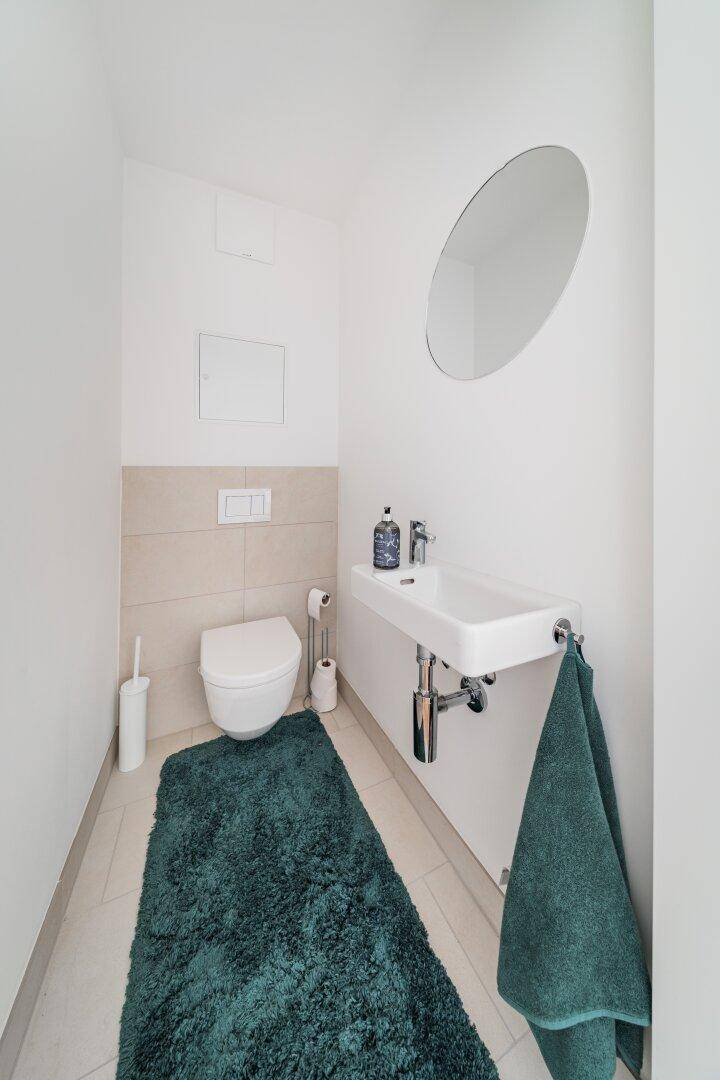 Kleines Gäste-WC mit Wand-WC, Handwaschbecken und modernen Fliesen.