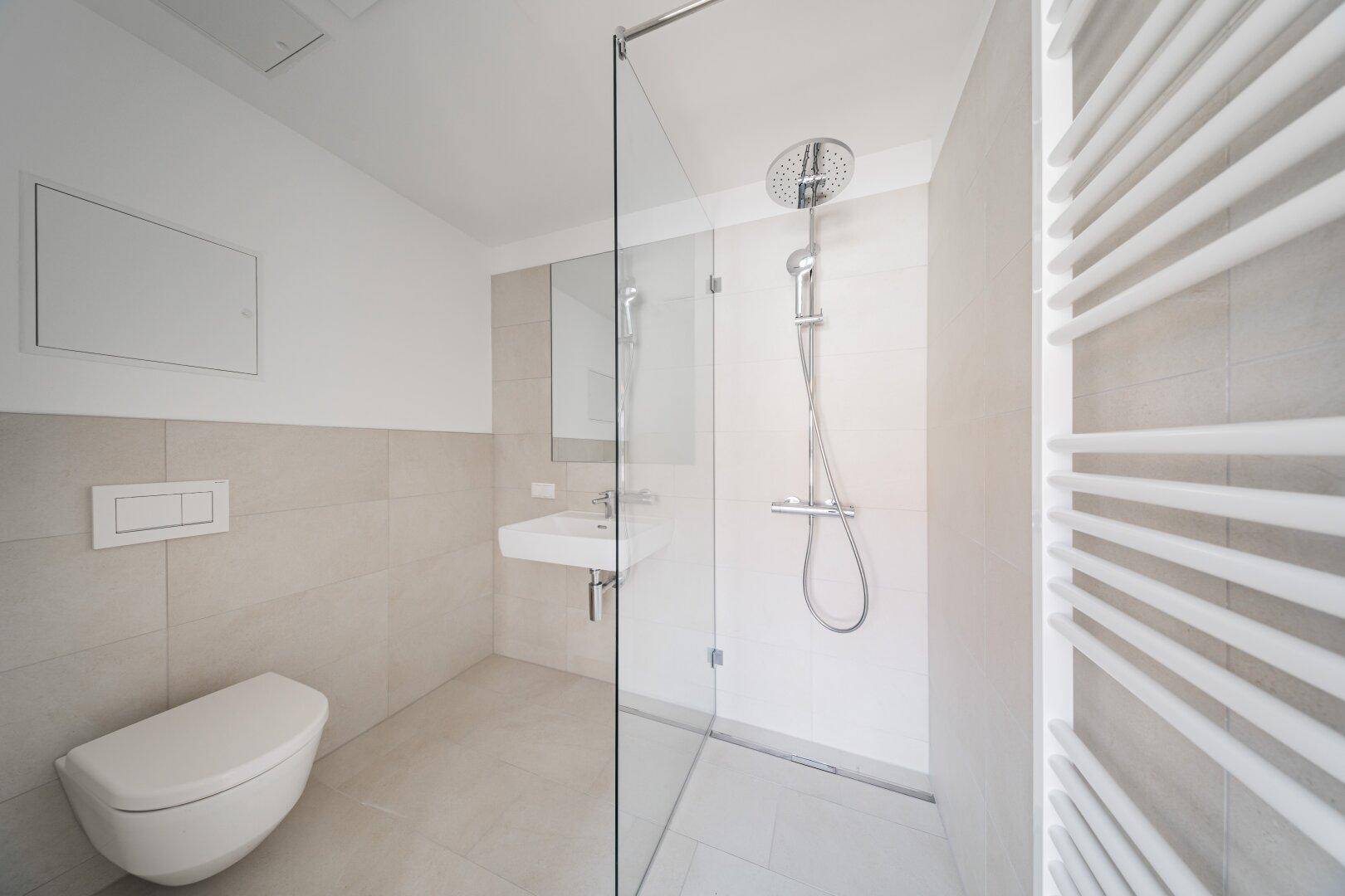 Modernes Badezimmer mit ebenerdiger Dusche, Wand-WC und beheiztem Handtuchhalter in hellen Fliesen.