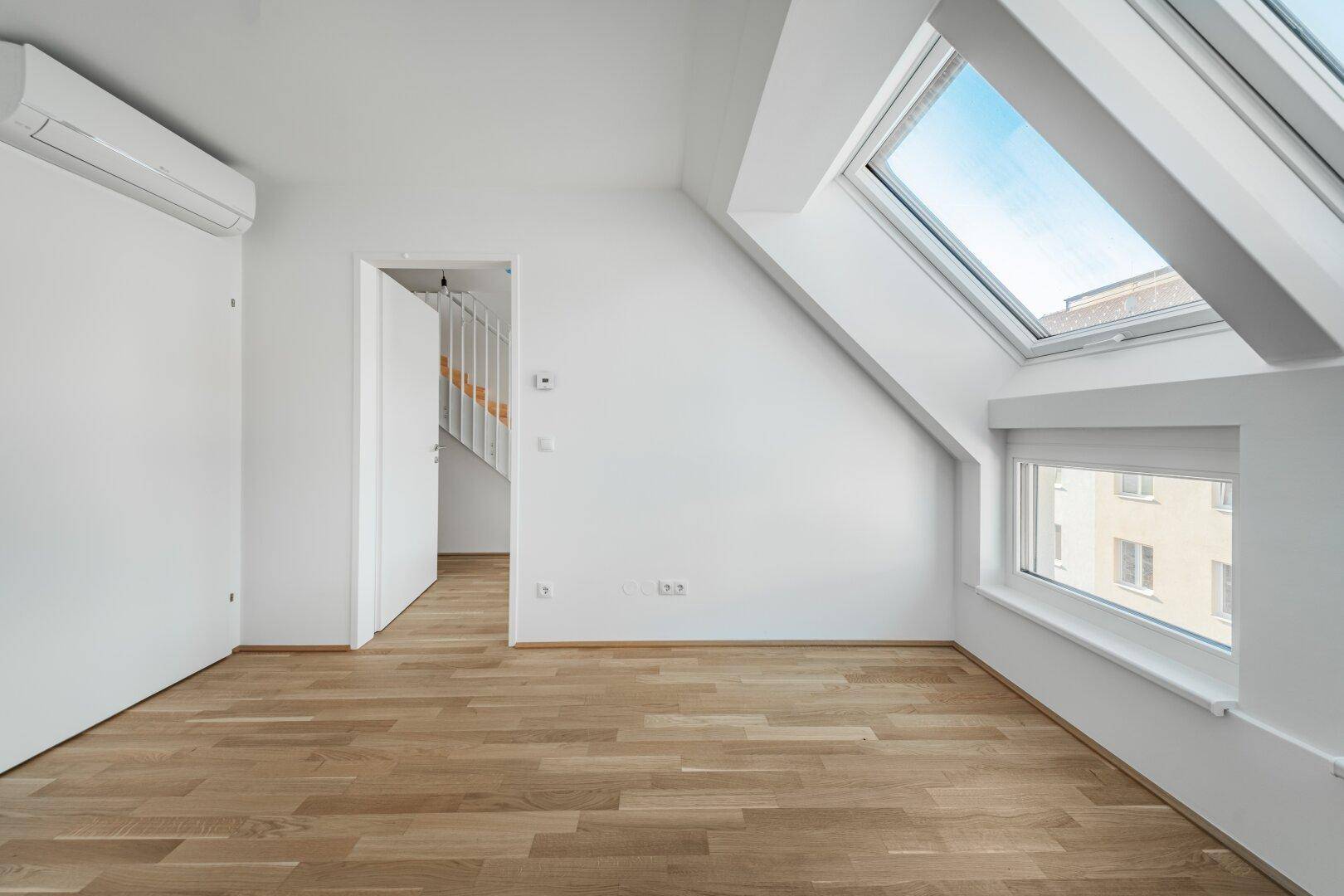 Geräumiges Dachzimmer mit Parkettboden, Klimaanlage und großem Dachfenster für viel Tageslicht.