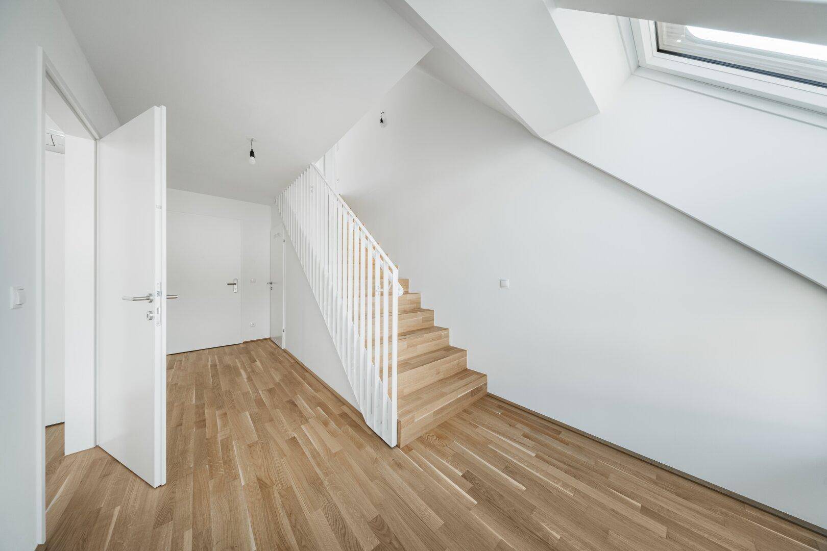 Heller Flurbereich im Dachgeschoss mit Holztreppe, Parkettboden und Zugang zu weiteren Räumen.