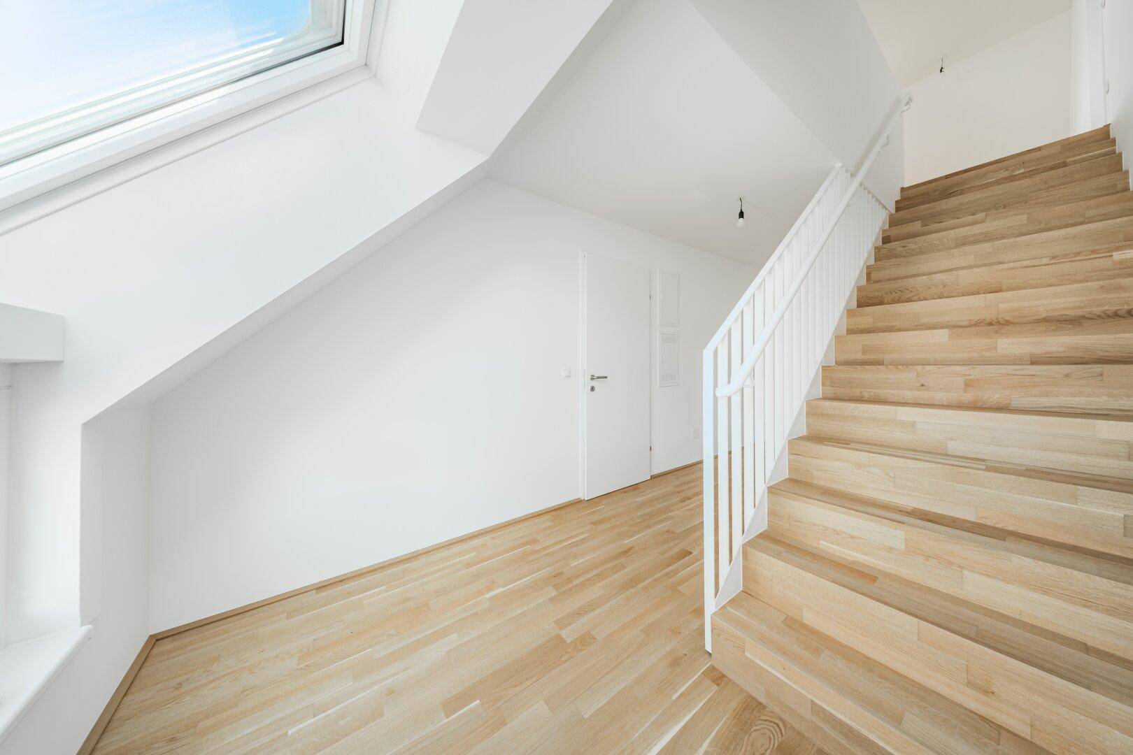Moderne Holztreppe mit weißem Geländer in einem hellen Flur, der zu den oberen Etagen führt.