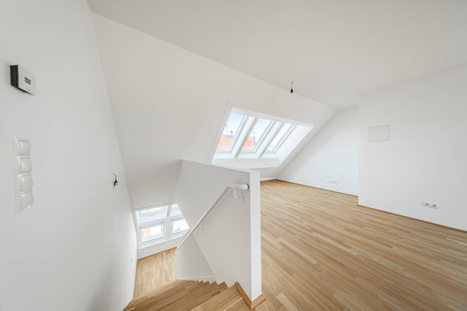 Helles Dachgeschoss mit Holztreppe, Parkettboden und großen Dachfenstern, die viel Licht hereinlassen.