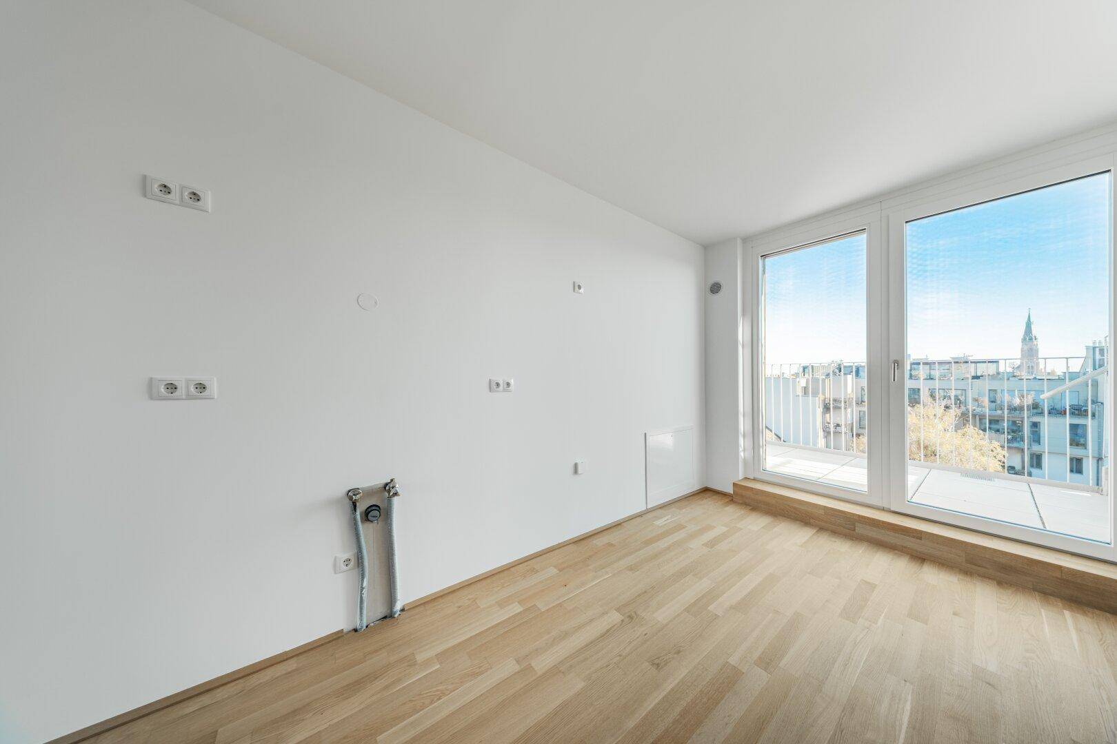 Heller Raum mit Parkettboden und großem Fenster, das Zugang zu einem Außenbereich bietet.