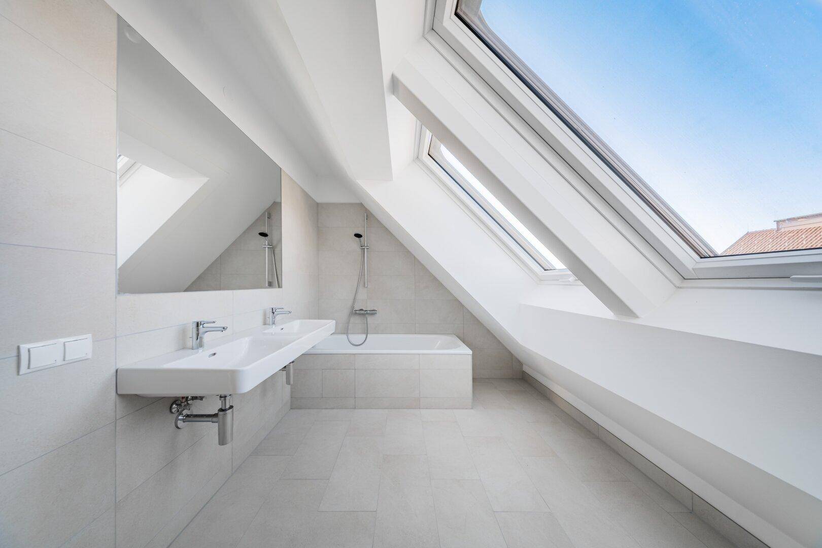 Modernes Badezimmer im Dachgeschoss mit Badewanne, Doppelwaschbecken und großen Dachfenstern.