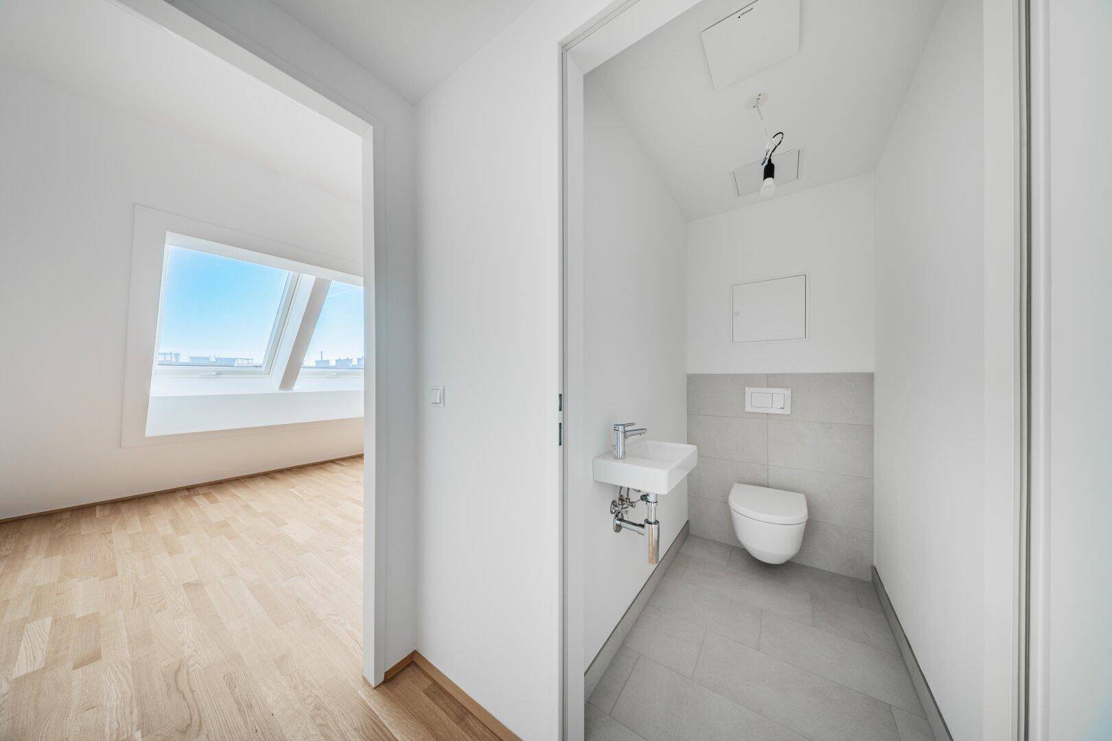 Kompaktes Gäste-WC mit modernem Wand-WC und kleinem Waschbecken in hellen Fliesen.