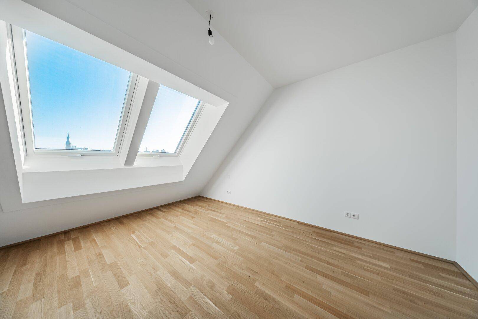 Geräumiges Dachzimmer mit Parkettboden und großen Dachfenstern, die den Raum mit Licht füllen.