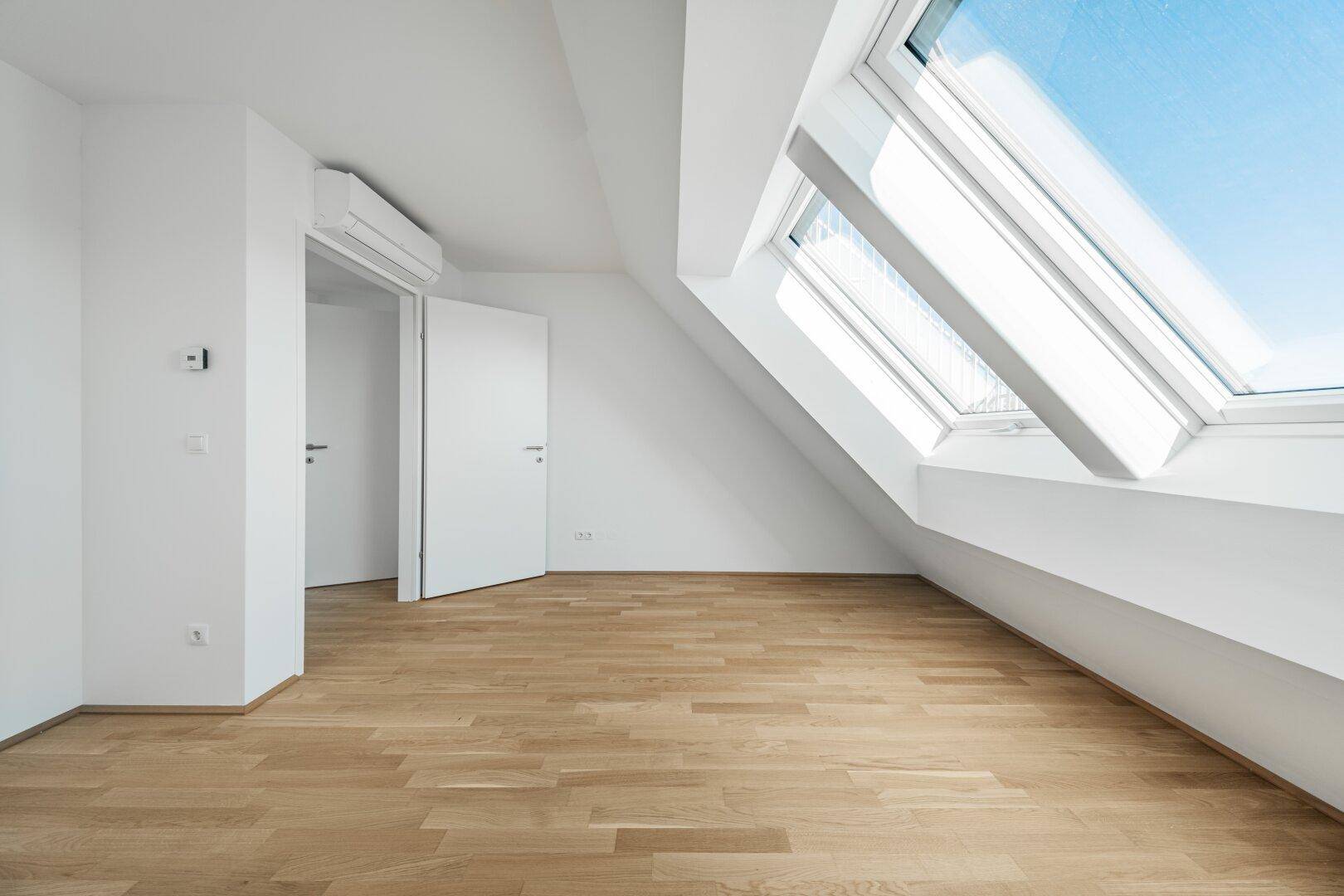 Heller Dachraum mit Parkettboden, Klimaanlage und großem Dachfenster, das viel Tageslicht bietet.