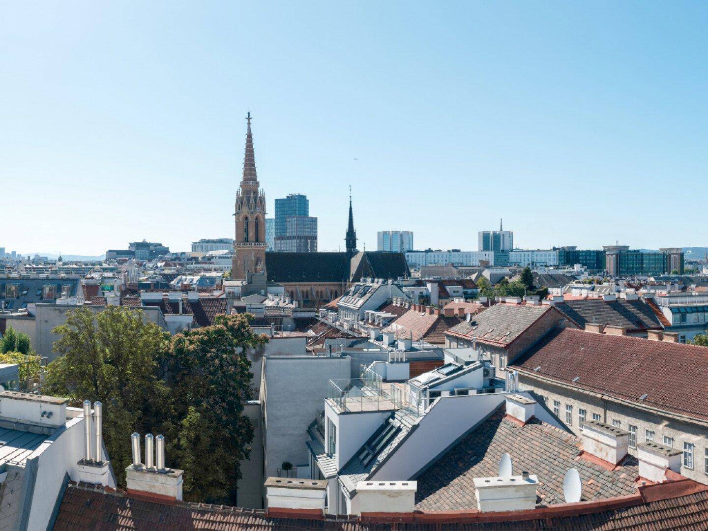 Panoramablick über die Dächer der Stadt mit historischen Gebäuden und modernen Türmen im Hintergrund.