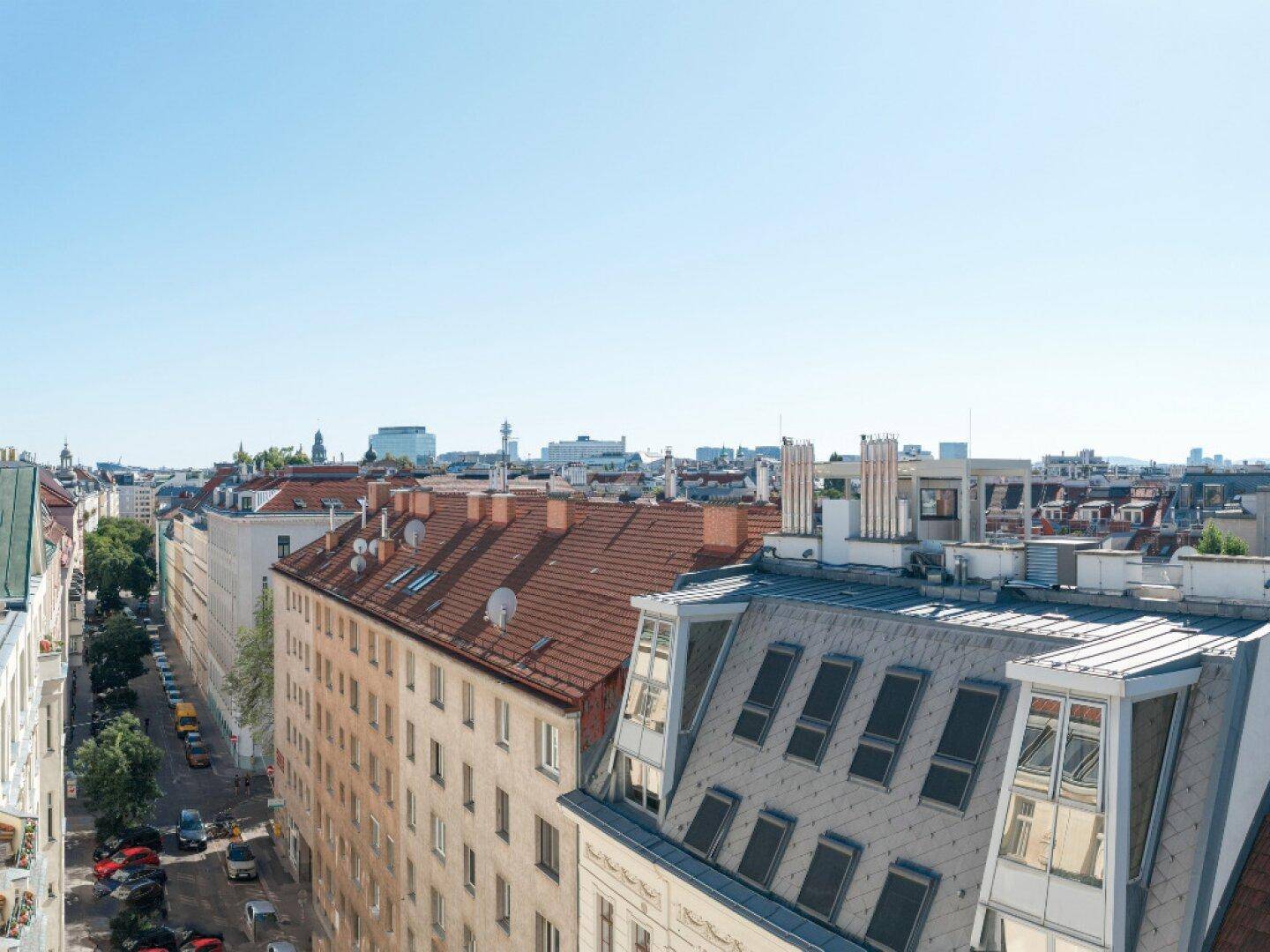 Weitläufiger Blick über die Dächer der Stadt mit einer belebten Straße und vielen Gebäuden.