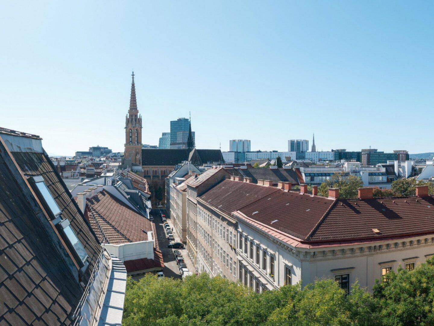 Panoramablick über die Dächer der Stadt mit einer Kirche und einer Mischung aus Alt- und Neubauten.