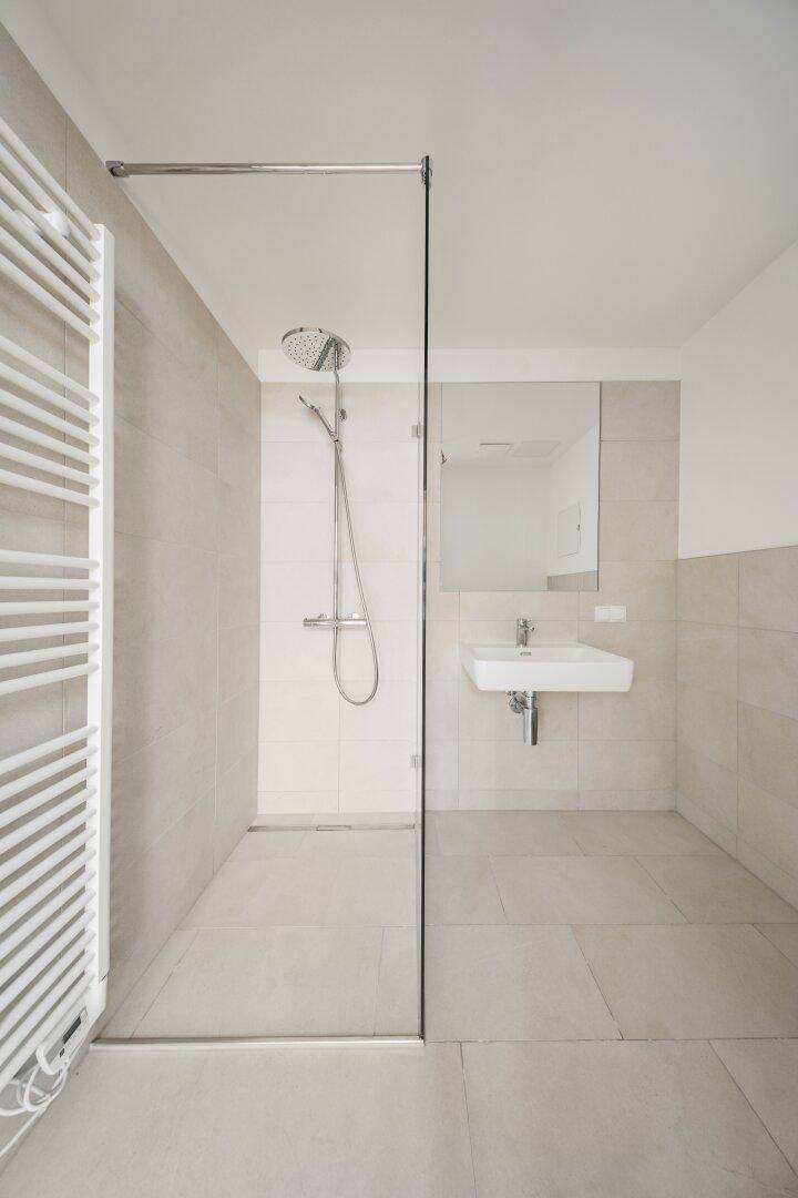 Modernes Badezimmer mit ebenerdiger Dusche, Wand-WC und beheiztem Handtuchhalter.
