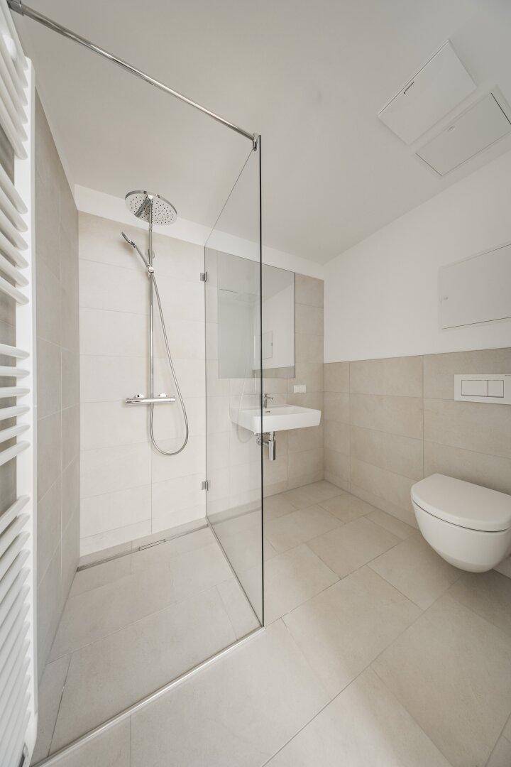 Modernes Badezimmer mit Fliesenboden, ebenerdiger Dusche, wandhängendem WC und Handtuchheizkörper.