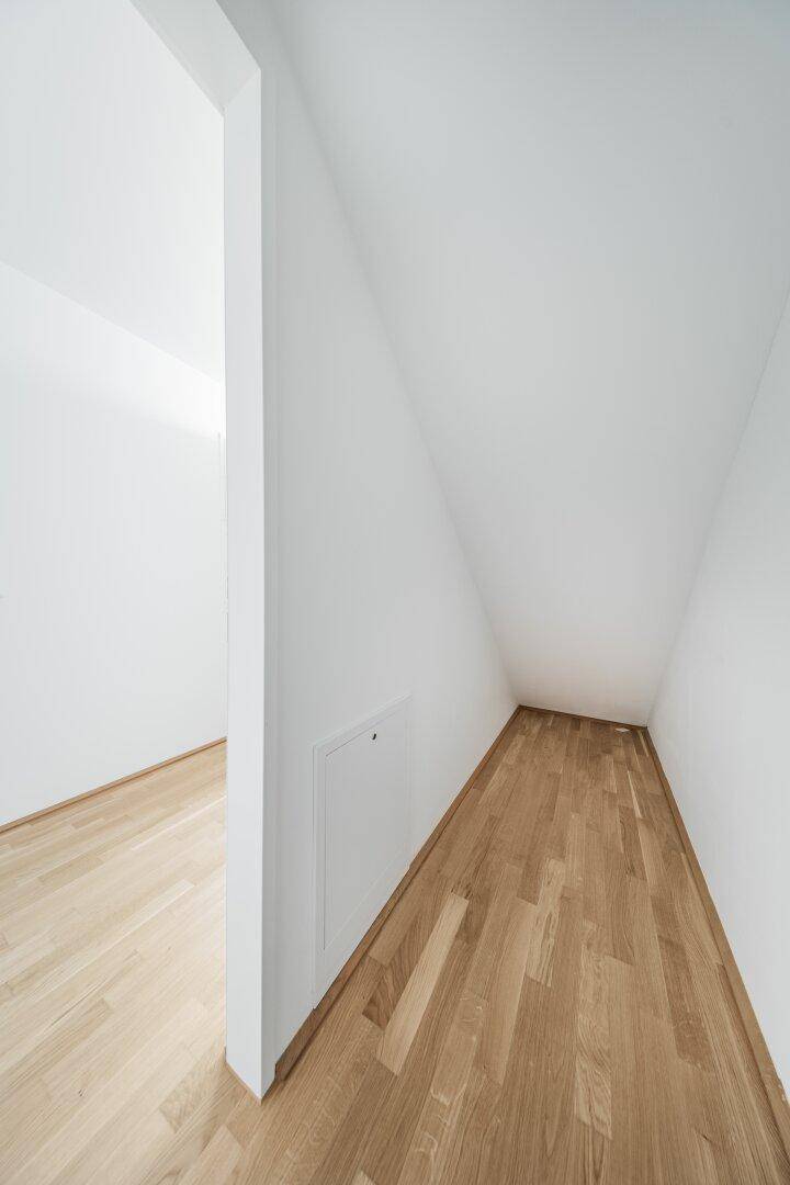 Praktischer Abstellraum unter der Dachschräge mit Holzboden und weiß gestrichenen Wänden.
