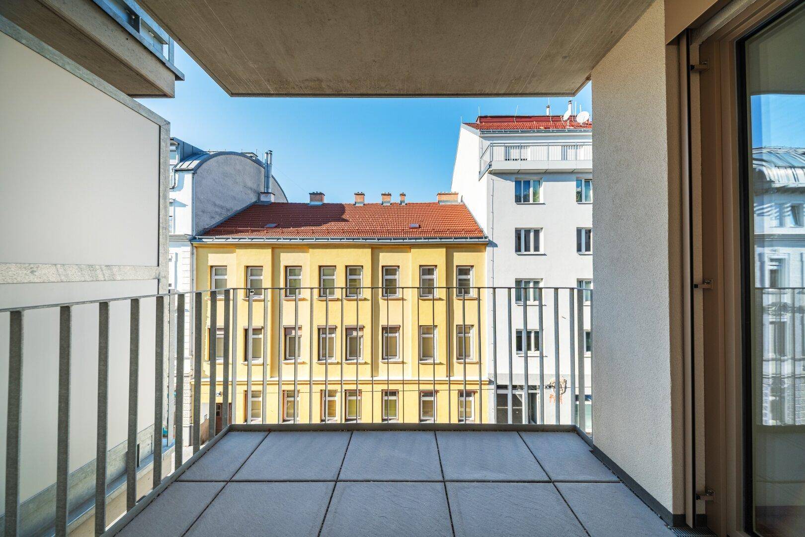 Heller Balkon mit Fliesenboden und Metallgeländer, mit Blick auf die umliegenden Gebäude.