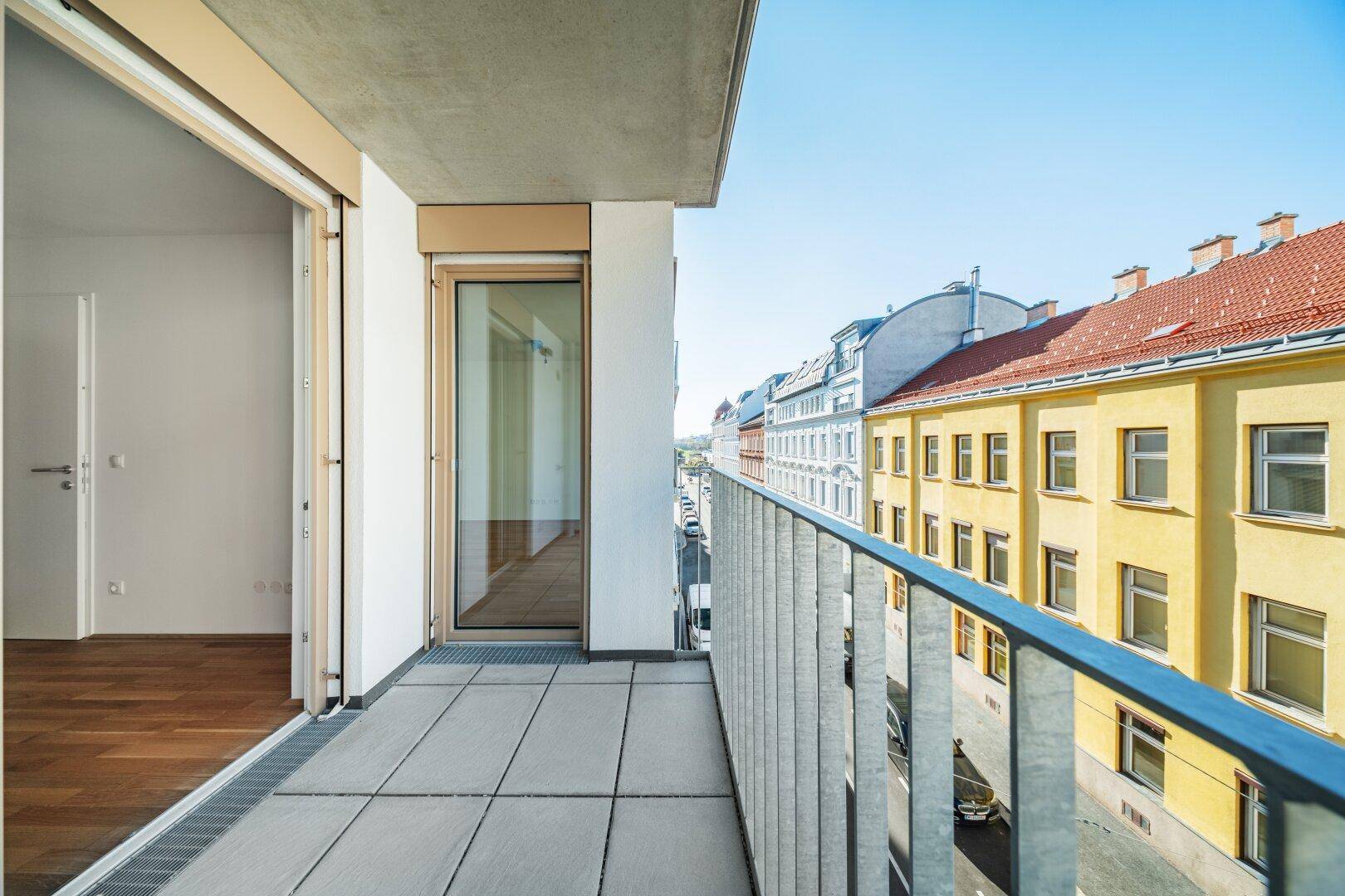 Langer Balkon mit Fliesenboden und Blick auf die belebte Straße und Gebäude.