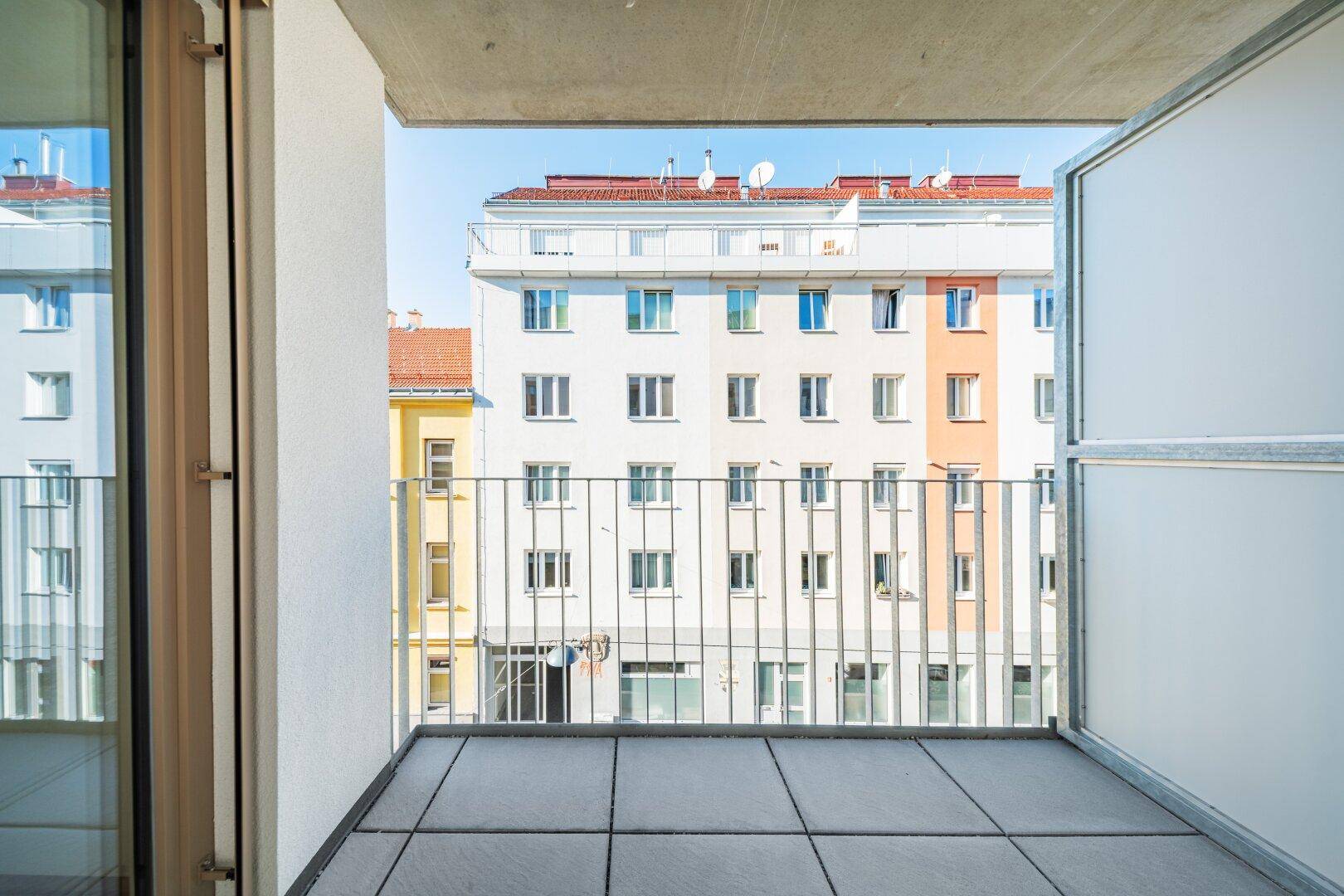 Geräumiger Balkon mit Fliesenboden und Metallgeländer, bietet Blick auf umliegende Gebäude.