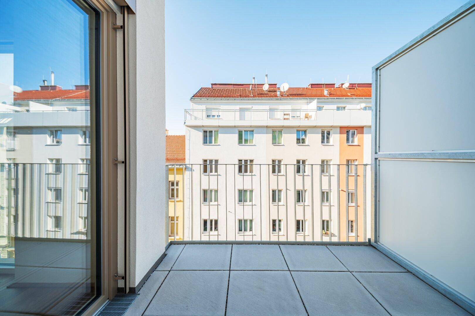 Geräumiger Balkon mit Fliesenboden und Blick auf die umliegenden Gebäude.