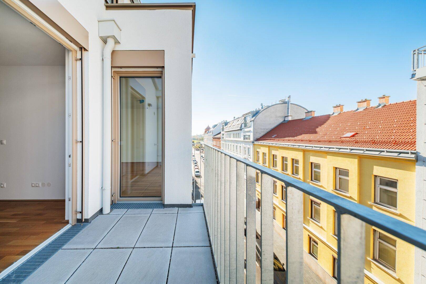 Langer Balkon mit Fliesenboden und weitem Blick entlang der Straße.