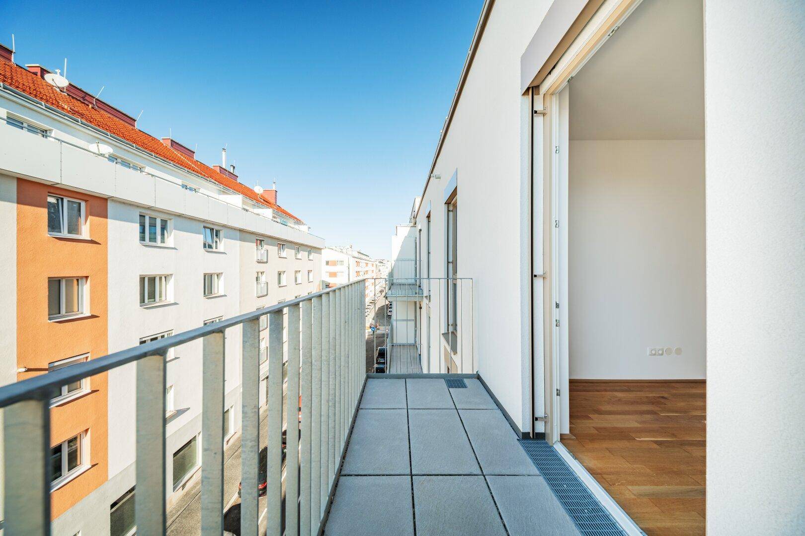 Schmaler Balkon mit Fliesenboden und Blick auf die Straße und angrenzende Gebäude.