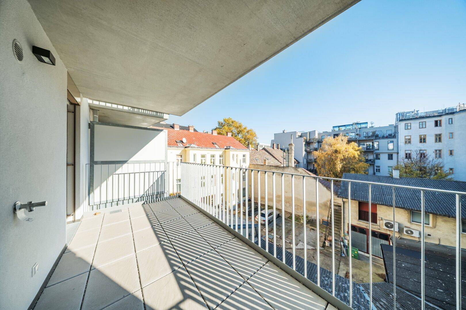 Geräumiger Balkon mit Fliesenboden und Blick auf die umliegenden Gebäude und den blauen Himmel.