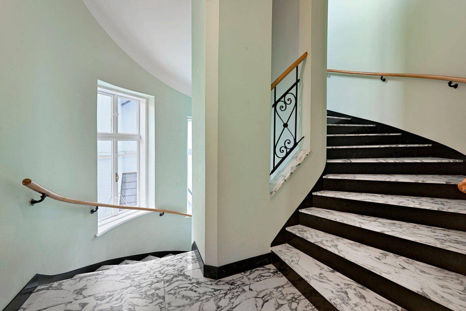 Elegantes Treppenhaus mit Marmorboden, geschwungener Treppe und schmiedeeisernem Geländer in einem Altbau.