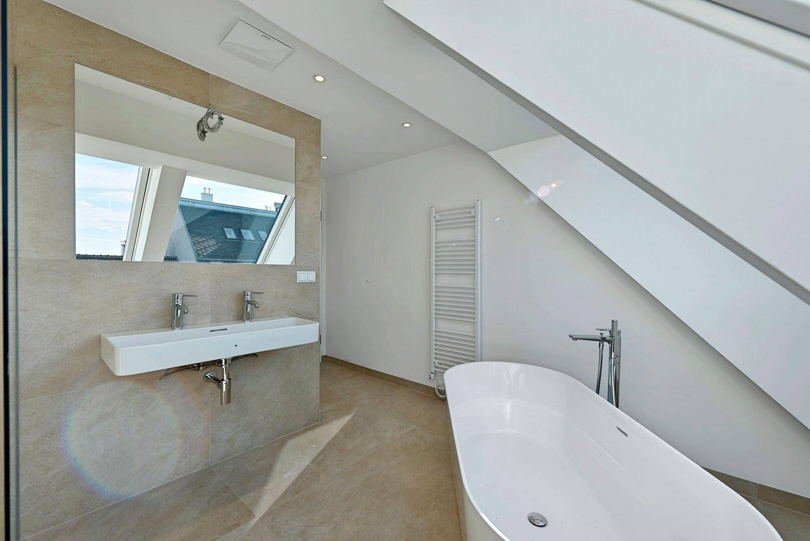 Geräumiges Badezimmer mit freistehender Badewanne, Doppelwaschbecken und beheiztem Handtuchhalter.