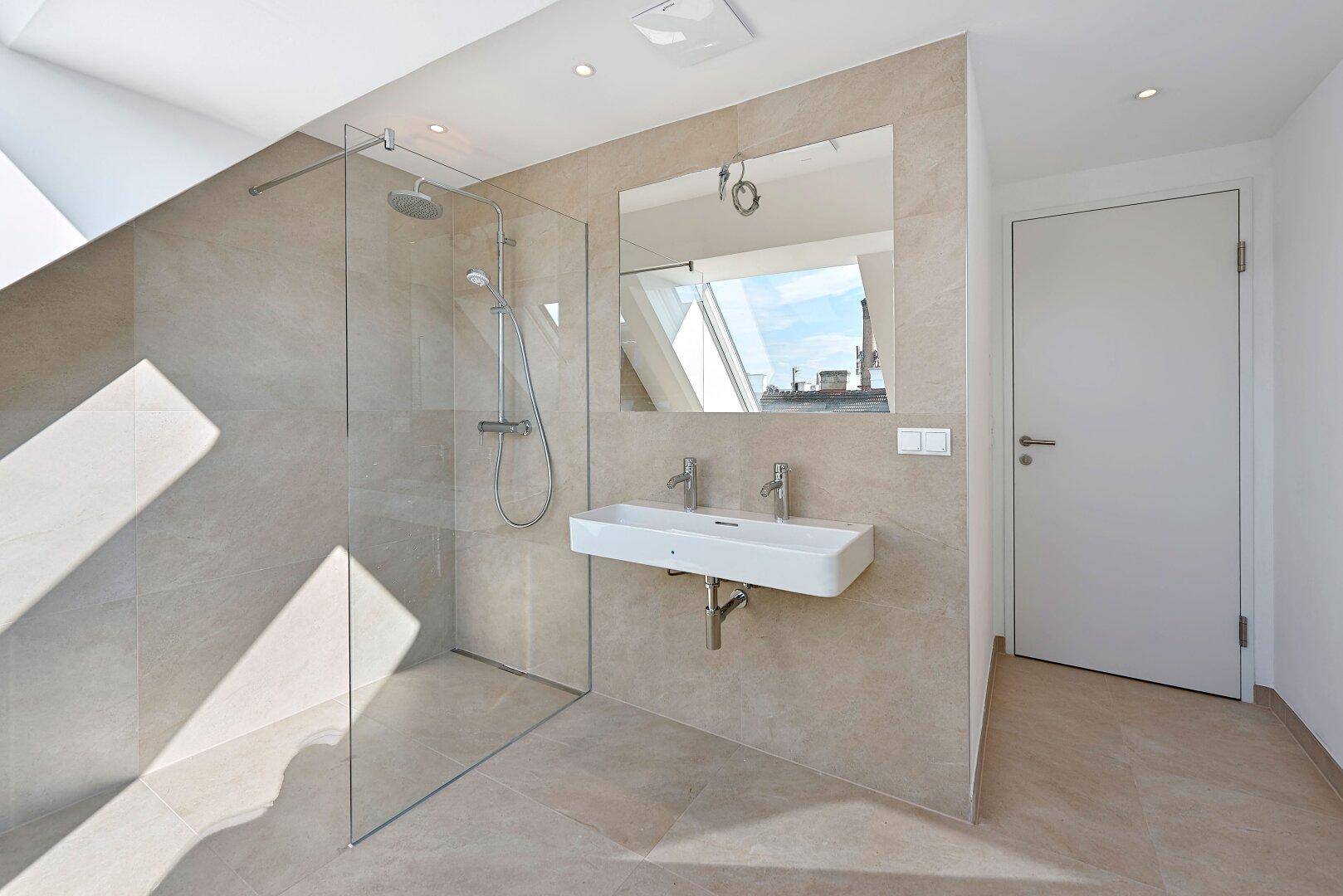 Modernes Badezimmer mit Doppelwaschbecken, großer begehbarer Dusche und Spiegel, der Tageslicht reflektiert.