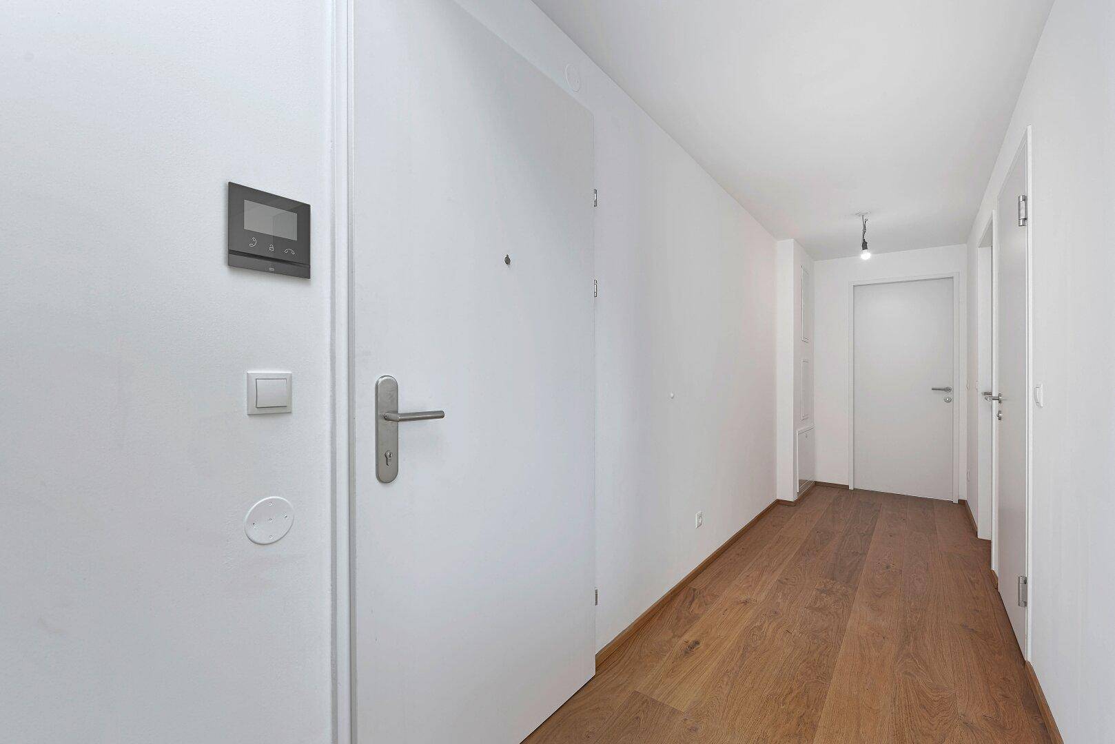 Heller Eingangsbereich mit Holzboden, weißen Türen und einer modernen Gegensprechanlage.
